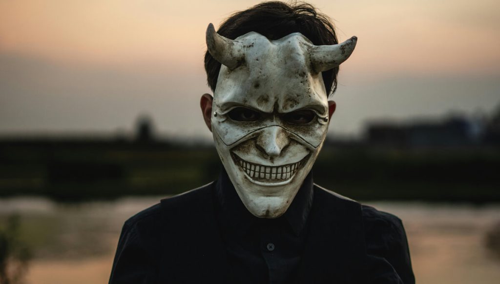 Man-at-sunset-wearing-smiling-white-devil-mask