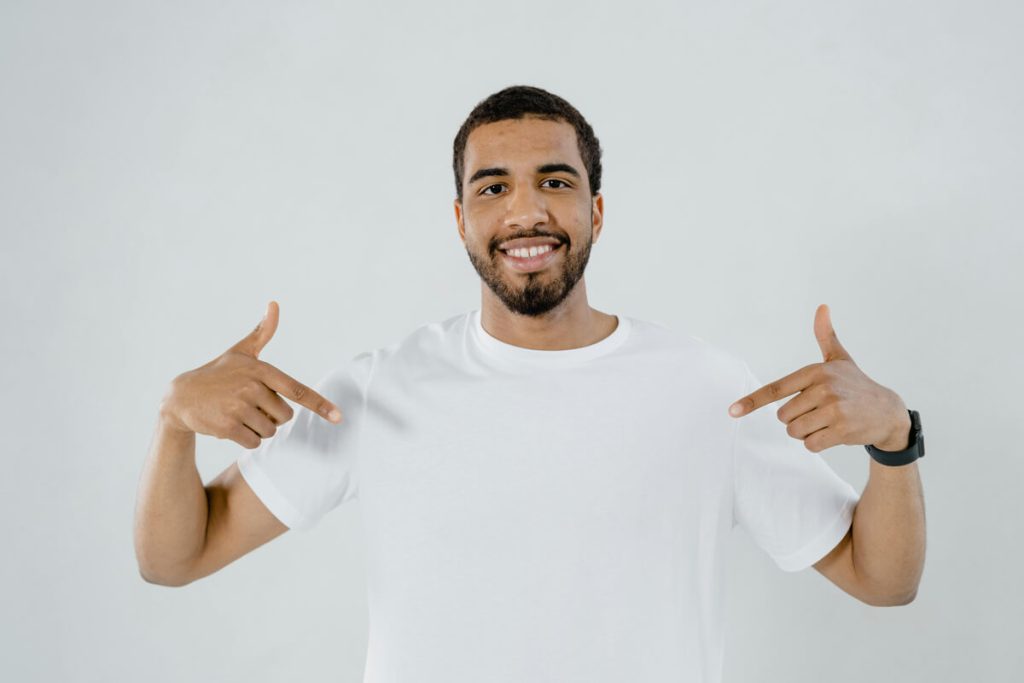 Smiling-man-dressed-in-white-with-both-hands-pointing-at-himself